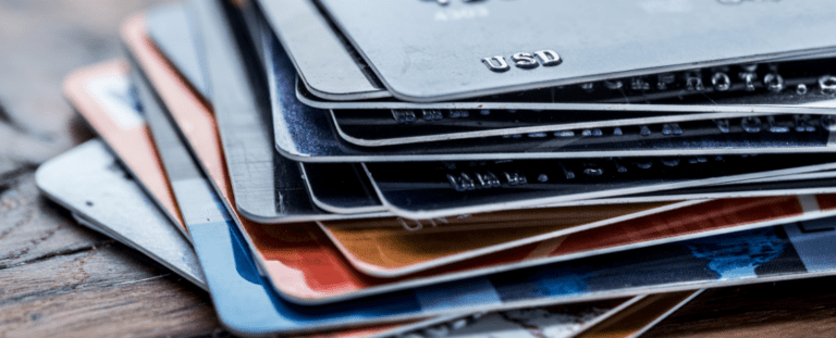 Nahaufnahme eines Stapels verschiedener Bank- und Kreditkarten auf einer Holzoberfläche. Symbolbild für nachhaltige Finanzprodukte, recycelte Bankkarten und umweltfreundliche Zahlungslösungen.