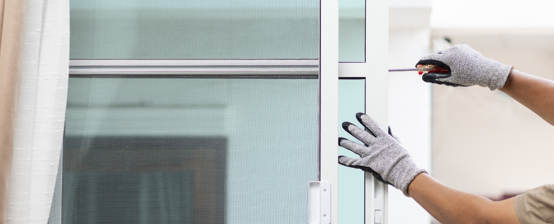 Handwerker mit grauen Arbeitshandschuhen montiert ein neues Fenster mit einem Schraubendreher. Das Fenster besteht aus einem weißen Aluminiumrahmen. Symbolbild für Modernisierung, Fenstertausch.